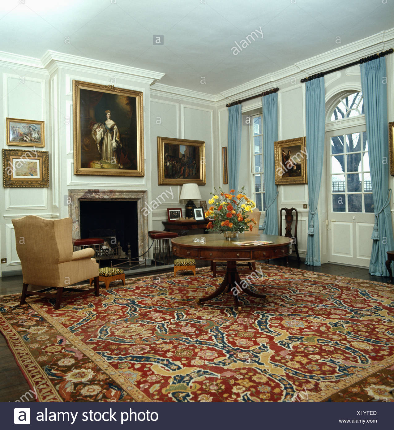 Runder Tisch Auf Gemusterten Roten Teppich Im Wohnzimmer Mit Bildern An Den Wanden Und Blauen Vorhangen An Den Fenstern Stockfotografie Alamy