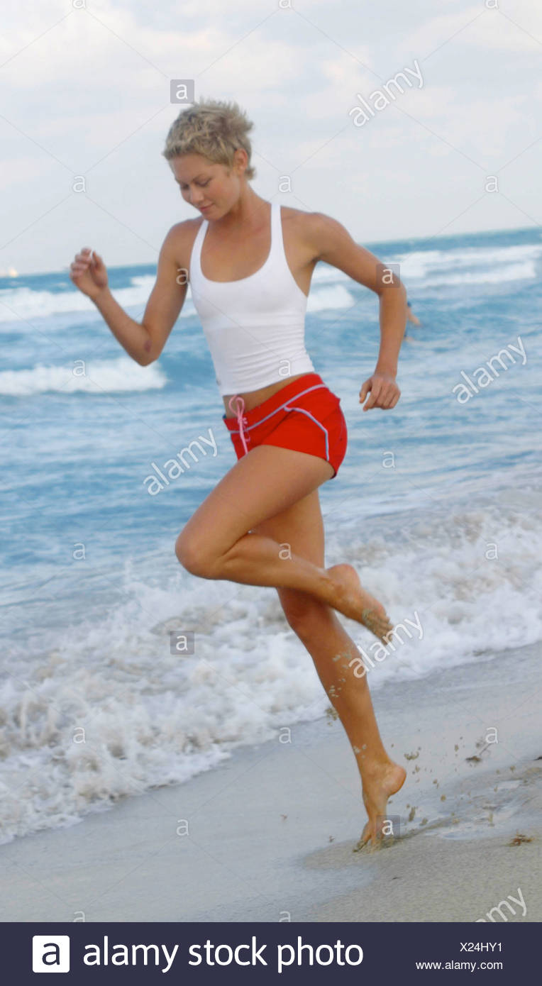 Weibliche Blonde Kurze Haare Tragen Weisse Weste Top Und Roten Hotpants Blau Trim Und Rosa Schleife Laufen Am Strand Am Rand Des Wassers Stockfotografie Alamy