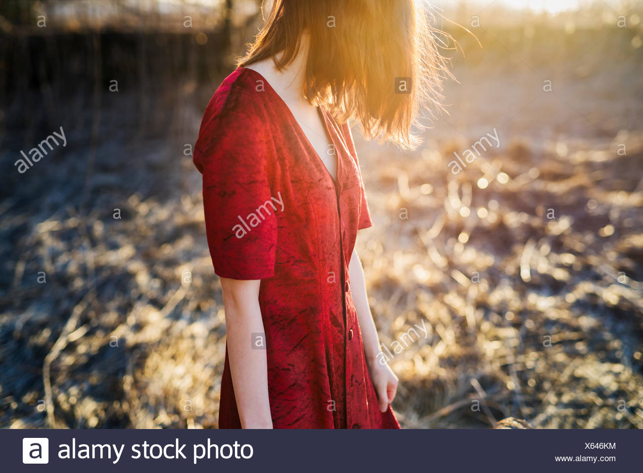 Finnland, Varsinais-Suomi, junge rote Haare Frau im roten Kleid stehen im Sonnenlicht Stockfoto