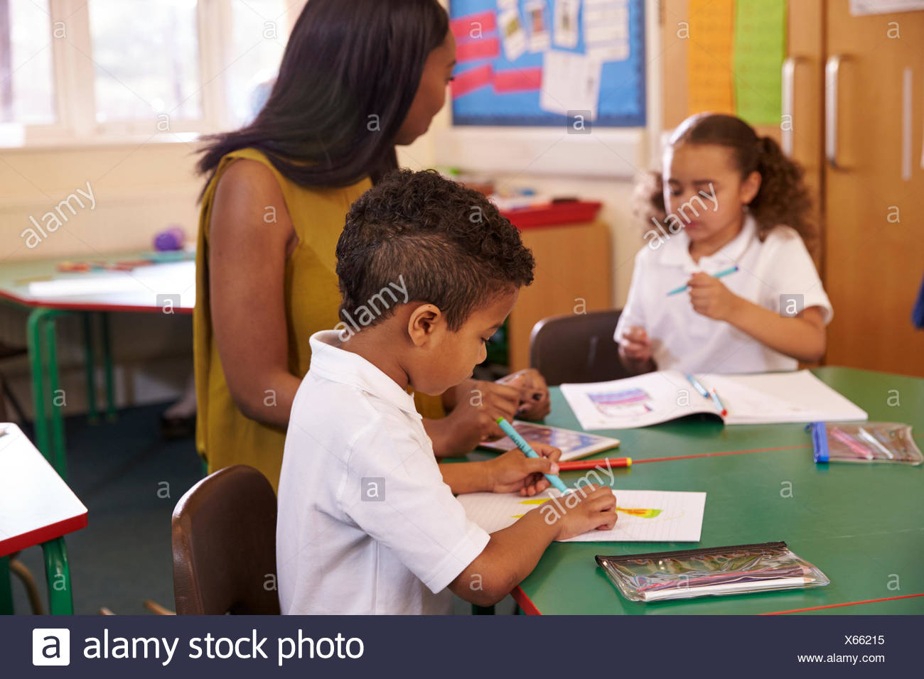 Weibliche Grundschullehrerin helfen Schülern am Schreibtisch Stockfoto