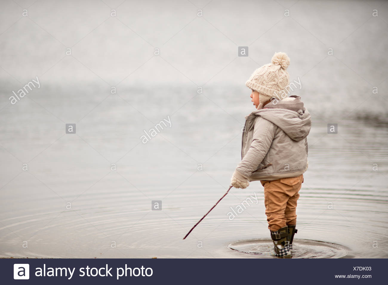 Kleiner Junge in einem See stehen, hält einen Stock Stockfoto