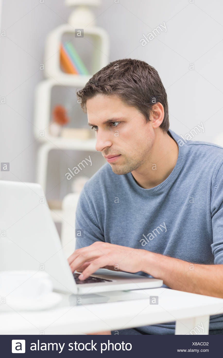 Ernster junger Mann mit Laptop im Wohnzimmer Stockfoto