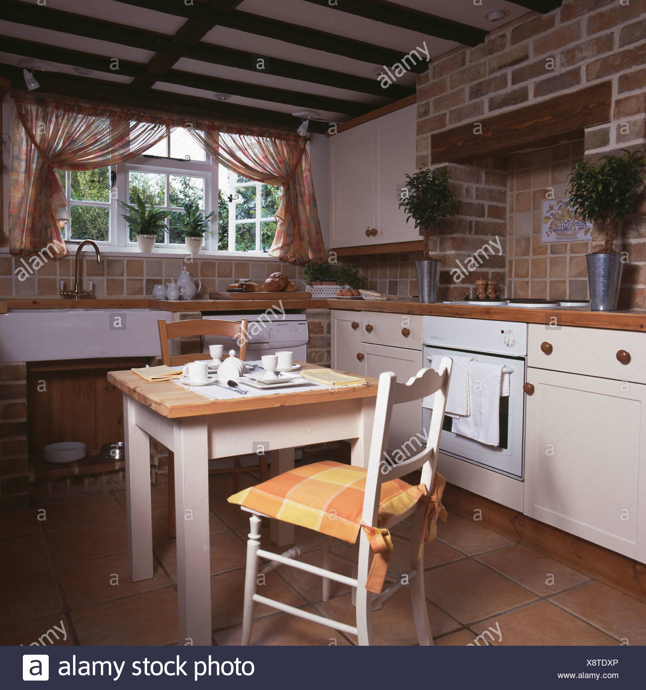 Weisse Holz Esstisch Und Stuhl Im Holzbalken Cottage Kuche Mit Eingebauten Weissen Einheiten Und Schier Floral Gardinen Am Fenster Stockfotografie Alamy
