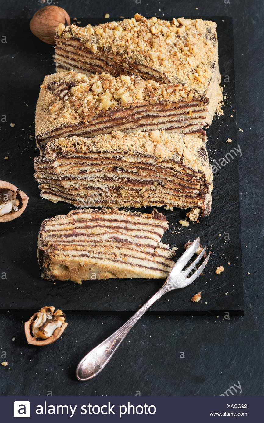 In Scheiben geschnitten hausgemachte Honigkuchen mit Schokolade Creme und Walnüsse, serviert mit Dessertgabel und gehackten Nüssen auf Schiefer Tafel. Nach oben Stockfoto