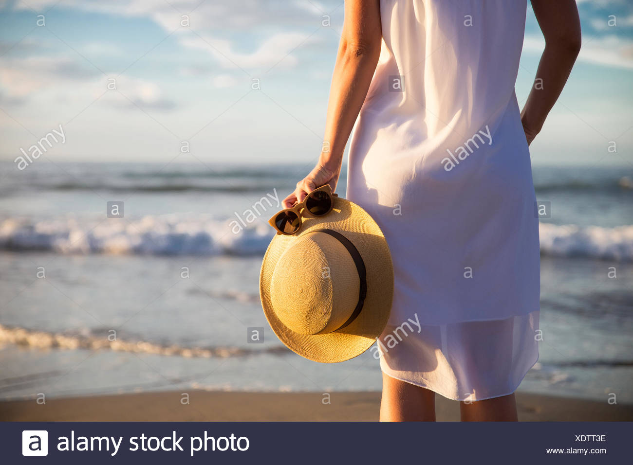 Rückansicht der Frau im weißen Kleid am Strand stehen und halten Hut Stockfoto