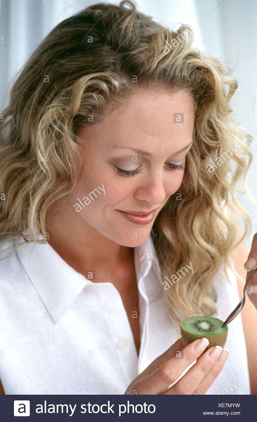 Frau Mit Lange Gewellte Blonde Haare Tragt Dezente Make Up Und Weisse Armellose Bluse Zu Kiwifrucht Mit Lachelnden Loffel Zu Essen Stockfotografie Alamy