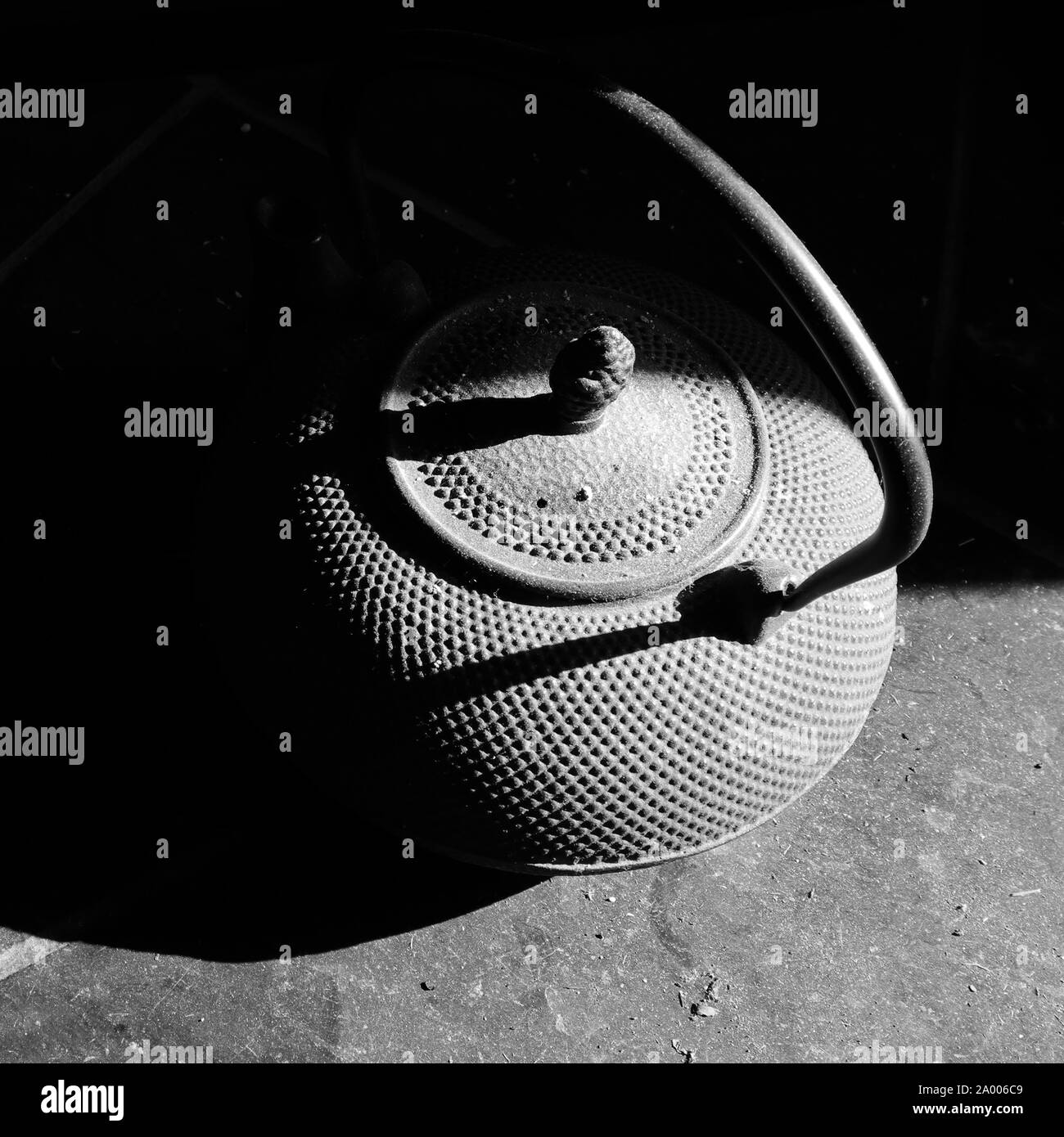 Tetera de hierro fundido negro sobre baldosas de pizarra sucio, cubierto de polvo, iluminada por la luz solar y se oculta en la sombra. Fotografía en blanco y negro. Foto de stock