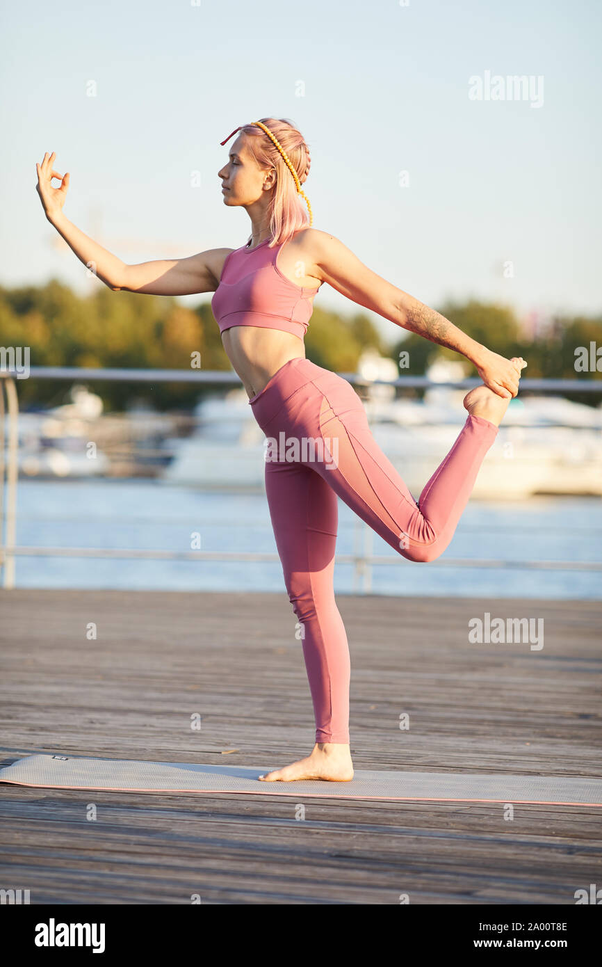 Colocar mujer en rosa la ropa deportiva de pie en pose y practicar yoga al aire libre en la ciudad Foto de stock