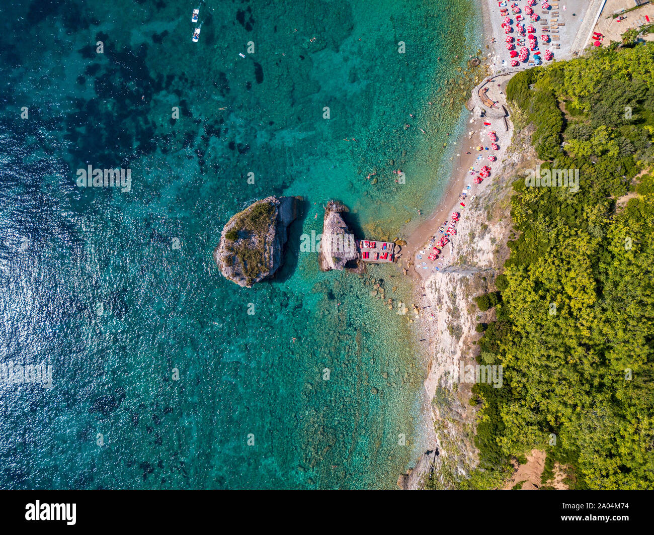 Vista aérea de Sveti Nikola, isla de Budva, Montenegro. Playa de Hawaii, sombrillas y bañistas y aguas cristalinas. Costas irregulares Foto de stock