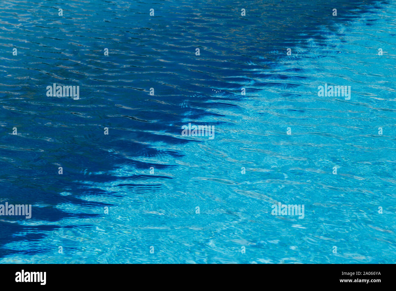 Una de dos colores, la luz y el agua azul oscuro con ondulaciones y reflejos en una soleada piscina. Foto de stock