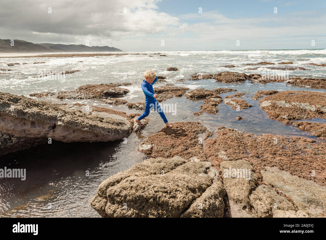 Boy pisando sobre las rocas en la costa de Nueva Zelanda Foto de stock