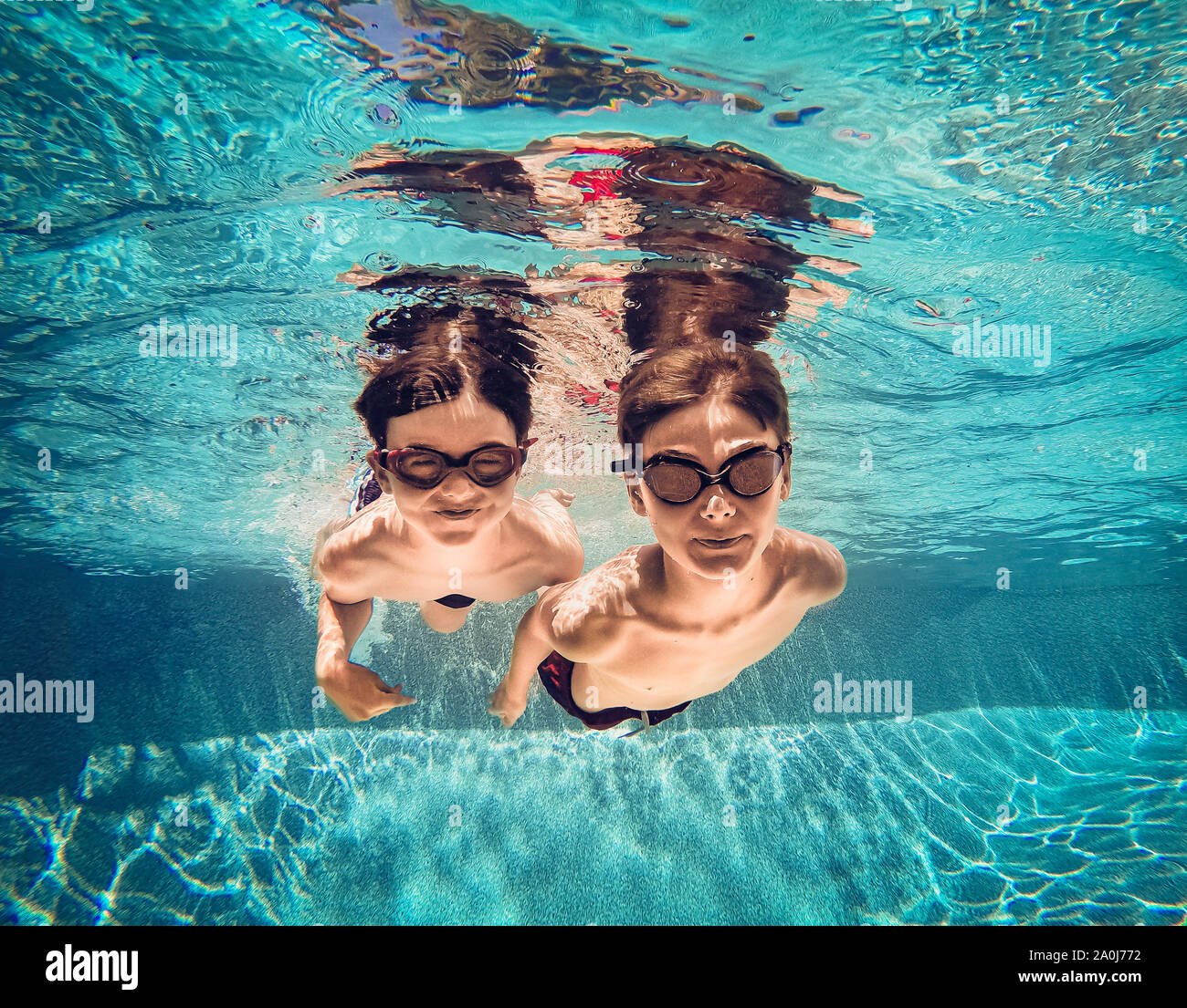 Imagen Submarina de dos niños nadando junto a otro en una piscina. Foto de stock