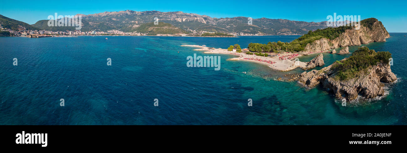 Vista aérea de Sveti Nikola, isla de Budva, Montenegro. Playa de Hawaii, sombrillas y bañistas y aguas cristalinas. Costas irregulares Foto de stock