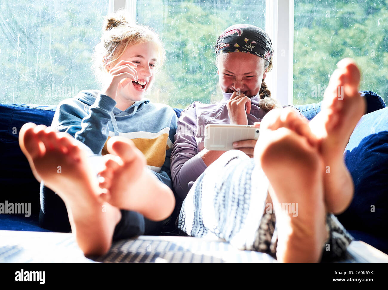 Las niñas adolescentes riendo en un sofá mirando algo en un teléfono Foto de stock