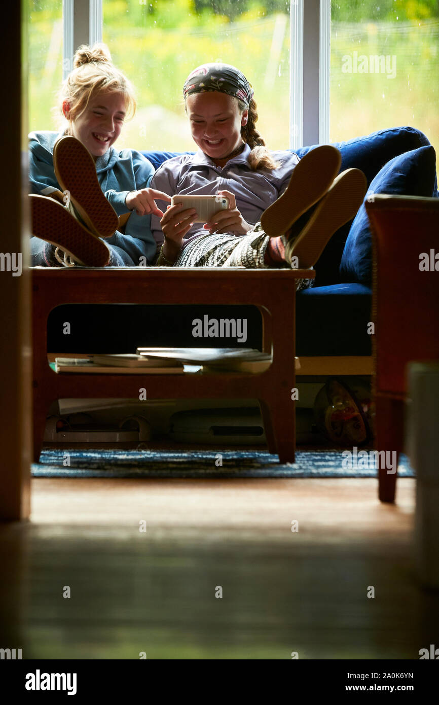 Las niñas adolescentes riendo en un sofá mirando algo en un teléfono Foto de stock