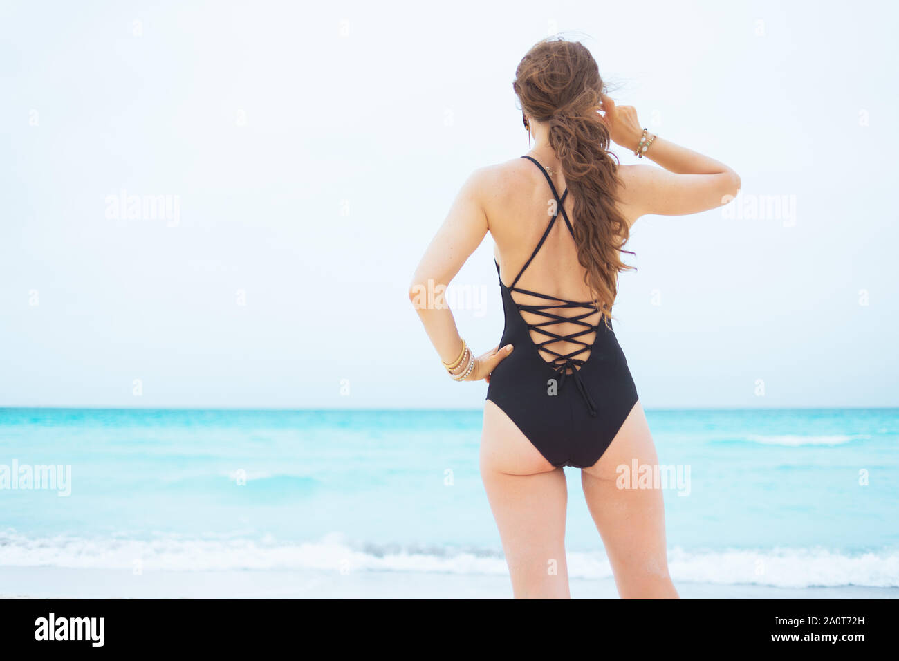 Visto desde detrás de la elegante mujer años con pelo rizado en elegante negro bañador en una playa blanca mirando en la distancia Fotografía de stock Alamy