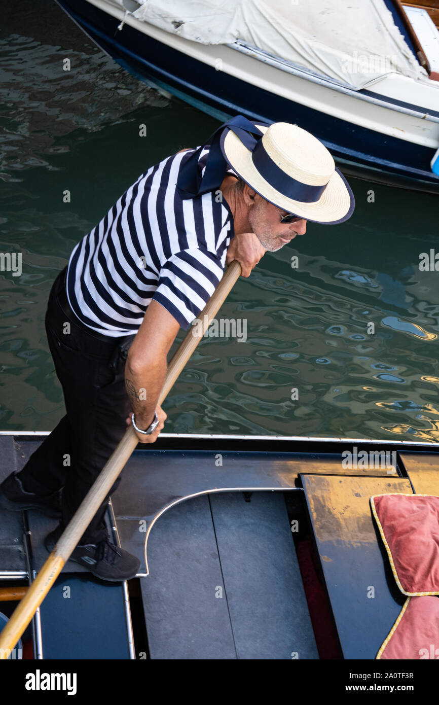 Un gondolero en tradicional camisa a rayas y sombrero de paja navegante en  una góndola por los canales de Venecia, Italia Fotografía de stock - Alamy