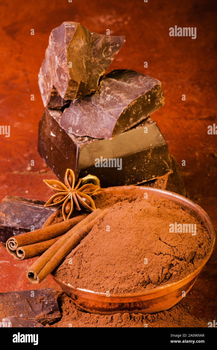 Recipiente con el polvo de cacao y trozos de chocolate oscuro en el fondo marrón Foto de stock