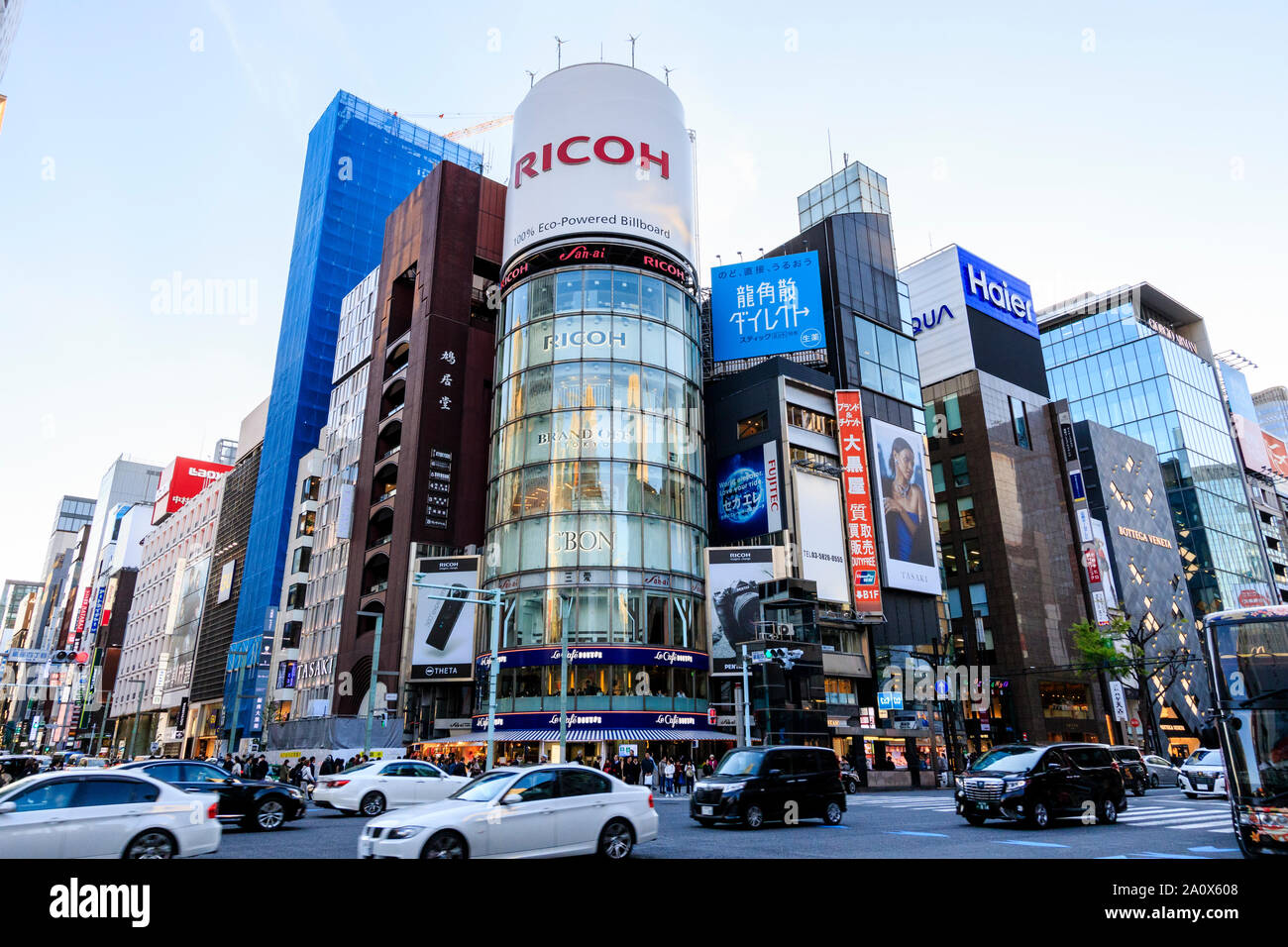 Tokyo, Ginza, en horario diurno. 4-chome intersección, autos pasando, con una fachada de vidrio San-ai, alias el EDIFICIO edificio de Ricoh, con su famoso billboard. Foto de stock