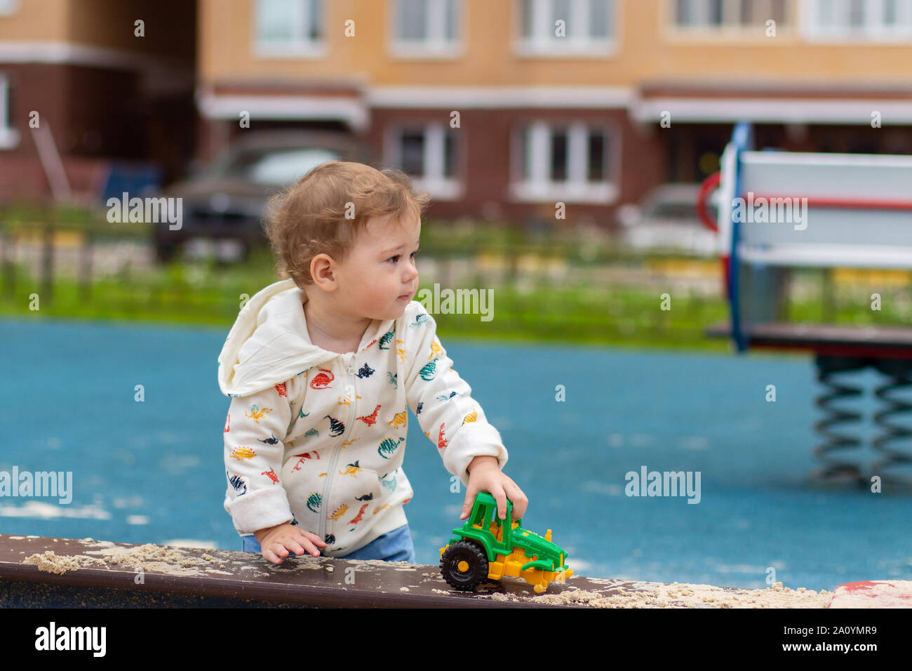 Bebé niña niño en una chaqueta blanca sobre un parque infantil piscina juega con un coche de juguete. Feliz Caucasian de 1 año de edad caminar en patio, puerto