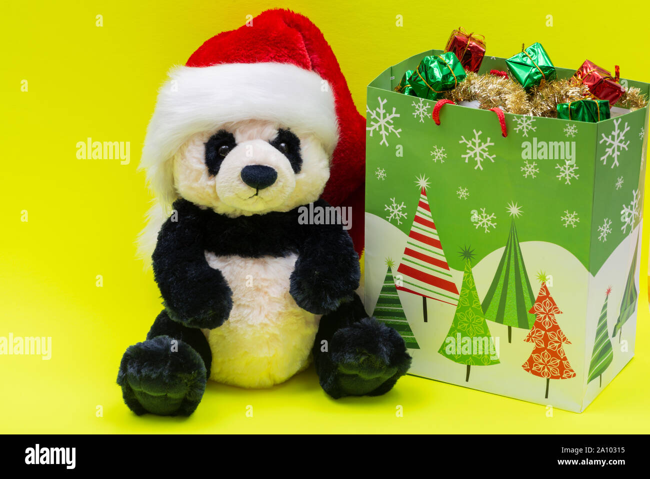 Bolsa con regalos y Oso Panda peluche llevar gorro de Papá Noel para  Navidad roja sobre fondo de color amarillo brillante. Navidad, Año Nuevo,  Vacaciones de invierno concepto Fotografía de stock -