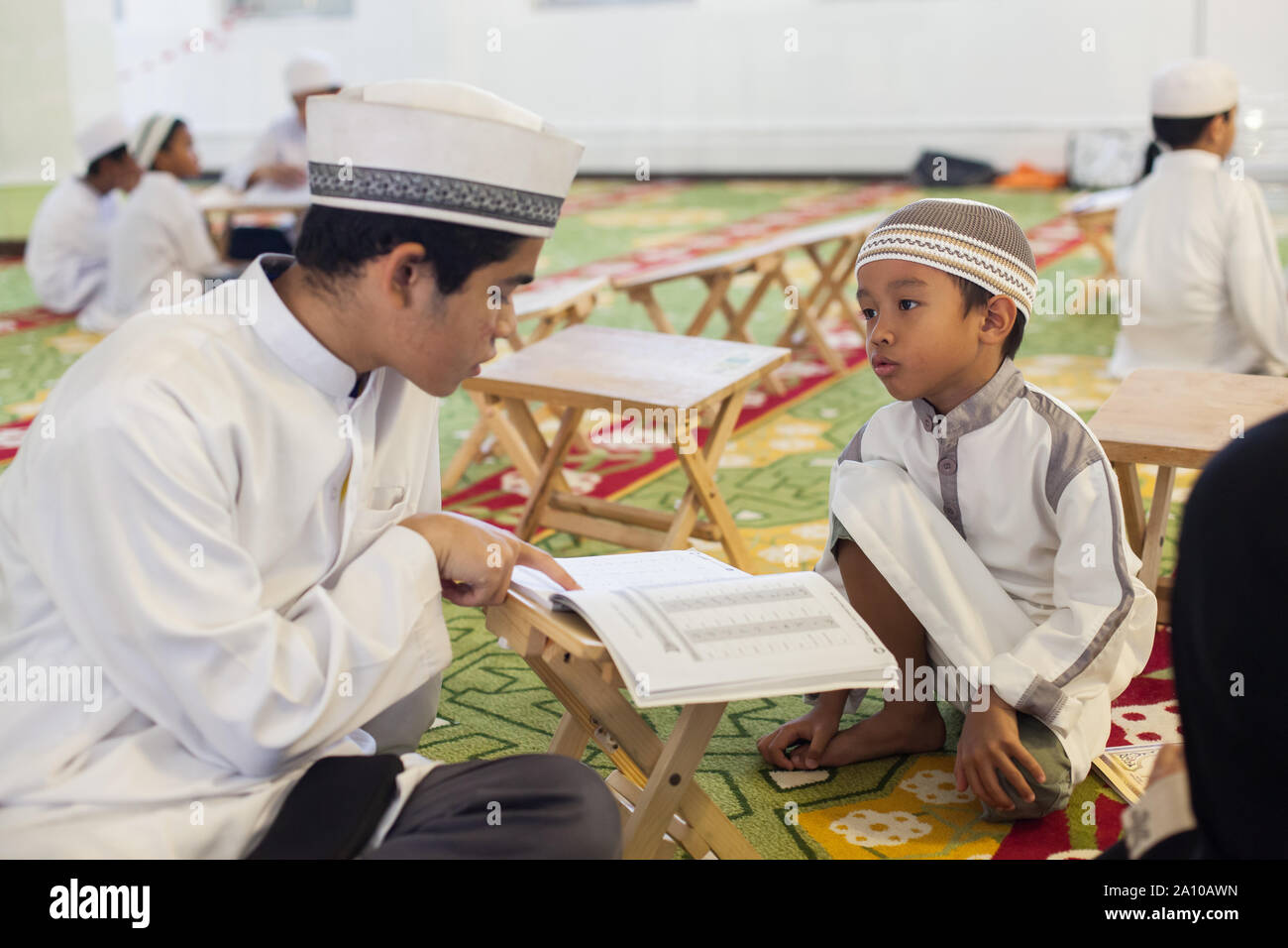 Un joven adolescente malaya enseñando a un niño muy joven estudiando dentro de Masjid Mezquita Sultan, Singapur Foto de stock