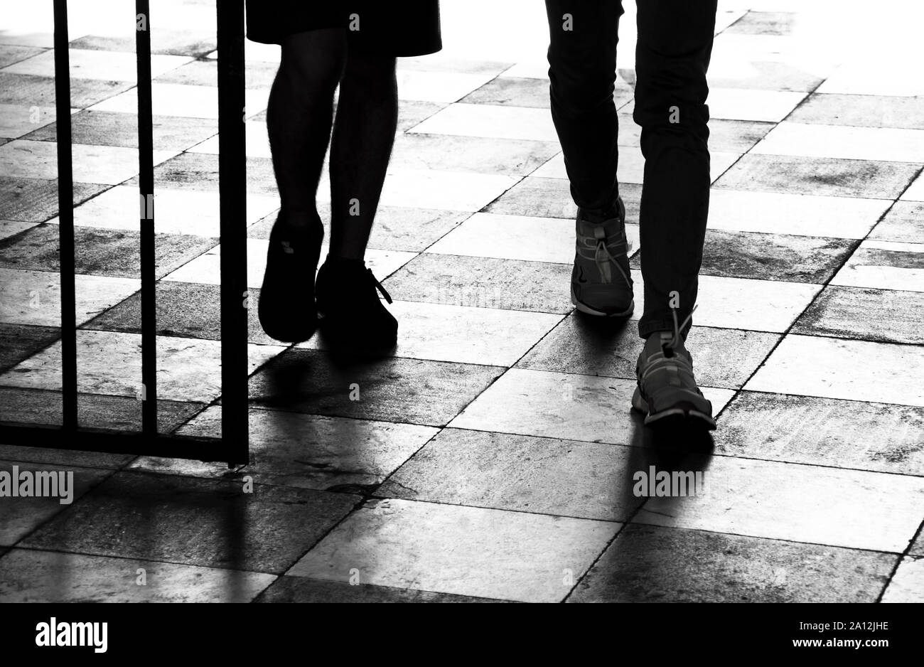 Silueta sombra de dos muchachos adolescentes caminando a través de la puerta; el detalle de las patas en blanco y negro de alto contraste Foto de stock