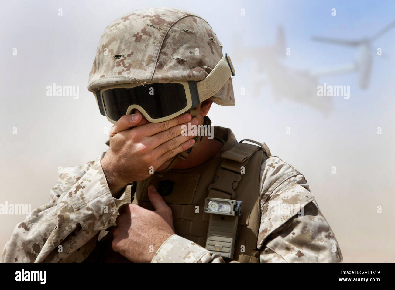 Un oficial de la naval protege su rostro de polvo por una MV-22 Osprey. Foto de stock