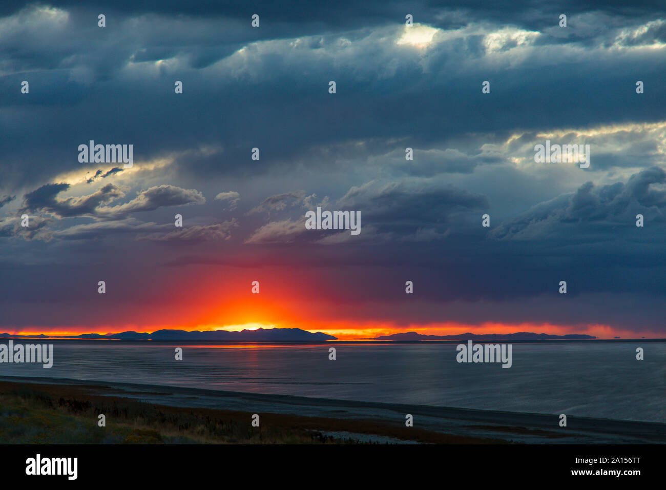 En esta foto el sol sobre las montañas de Lakeside lanza un resplandor en las amenazadoras nubes encima y reflexionando sobre el Gran Lago Salado. Foto de stock