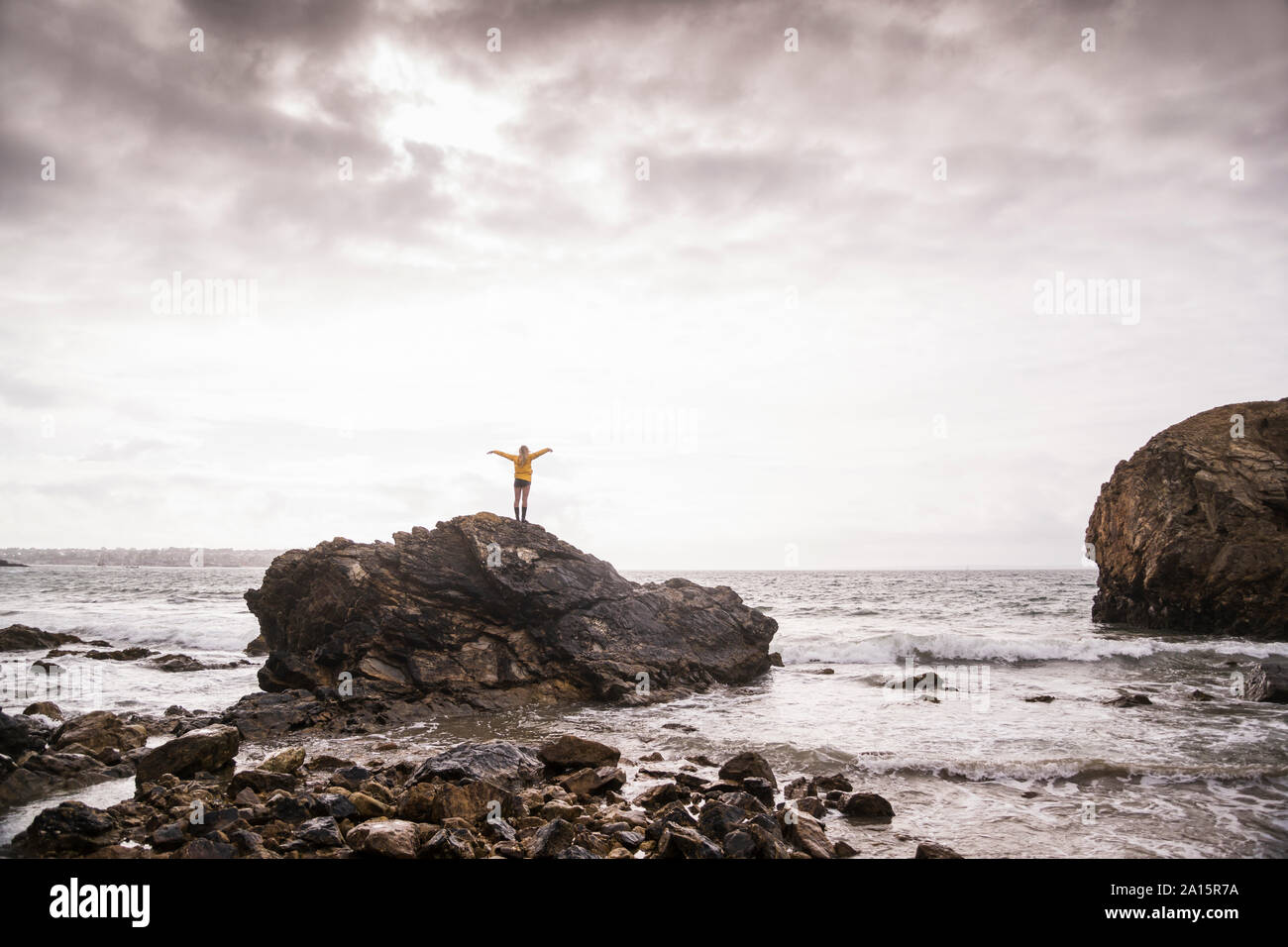 Vista trasera de mujer con brazos levantados, de pie en la playa rocosa Foto de stock