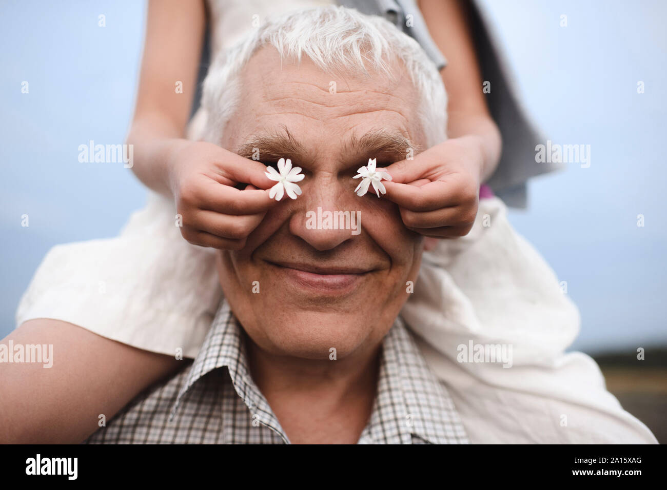 Manos de niña que cubren los ojos de su abuelo con flores blancas Foto de stock