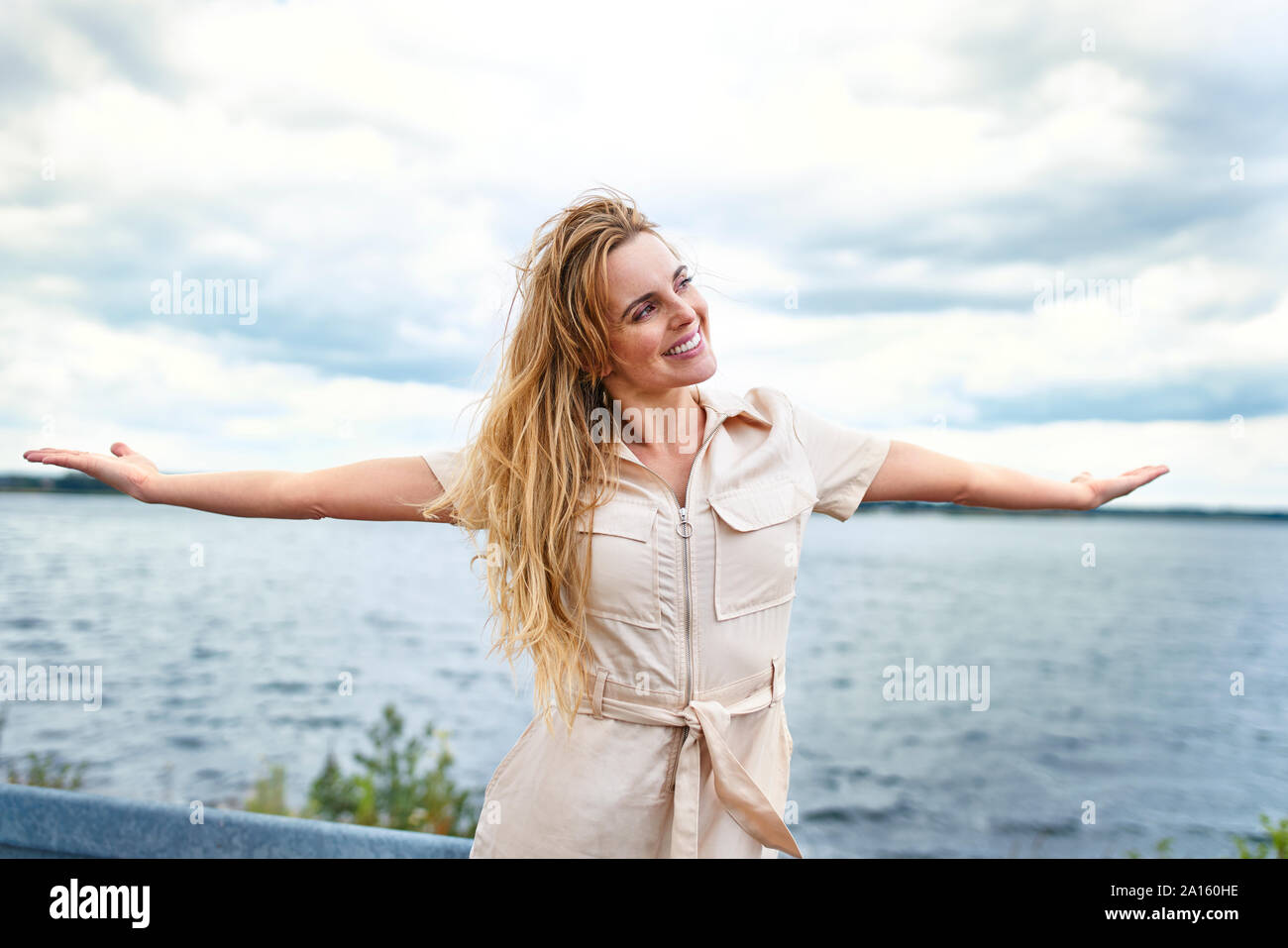 Feliz Mujer de pie en la orilla del lago con los brazos abiertos Foto de stock