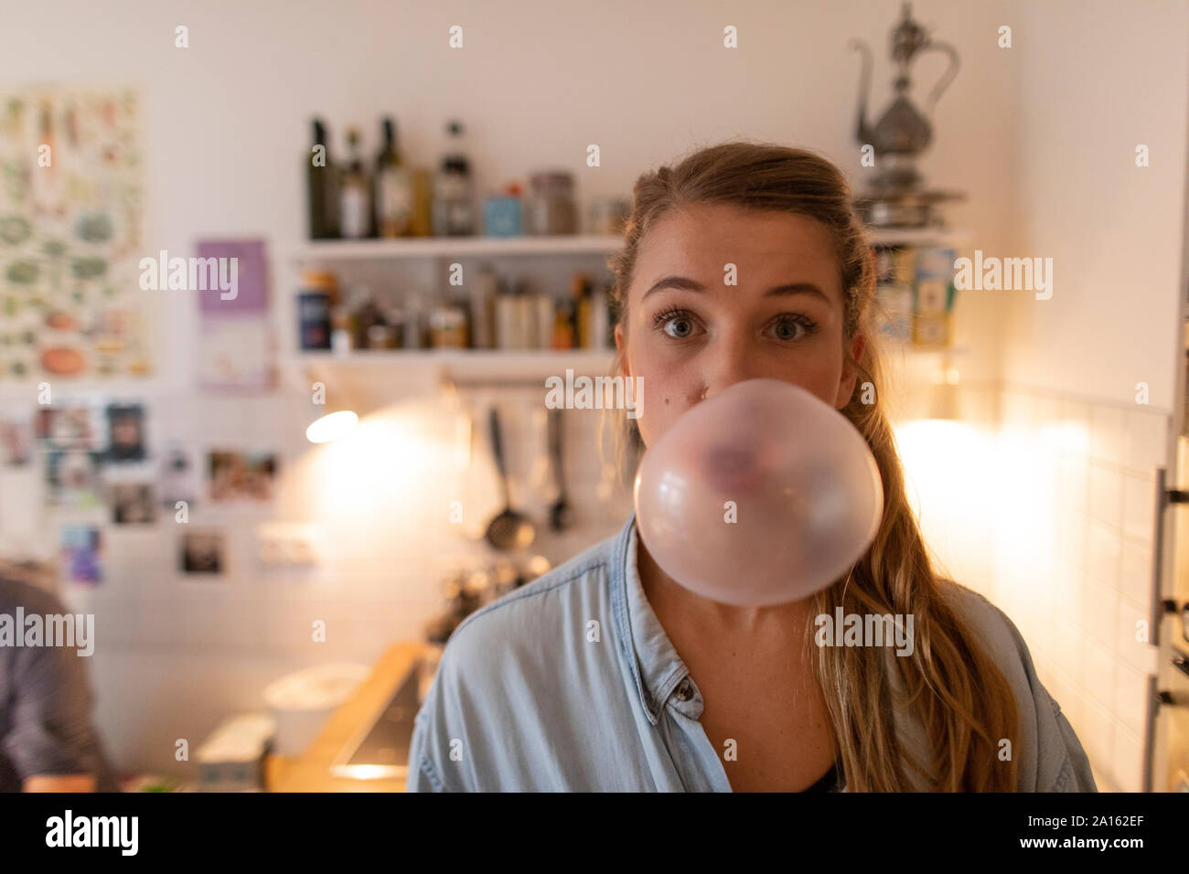 Mujer joven en la cocina de casa haciendo burbujas de chicle Foto de stock