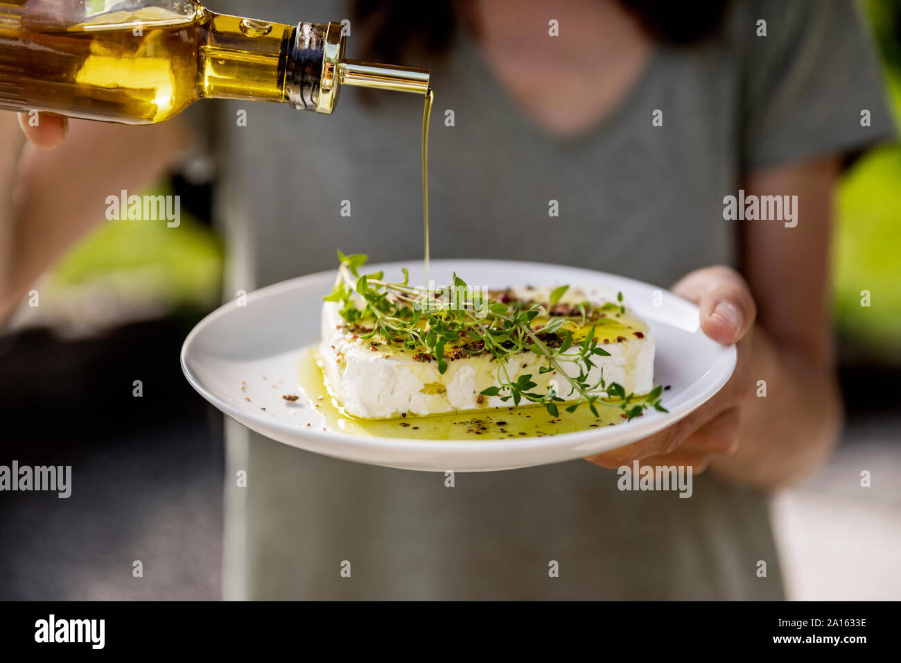 Close-up de mujer vertiendo aceite de oliva en el plato de queso de oveja Foto de stock