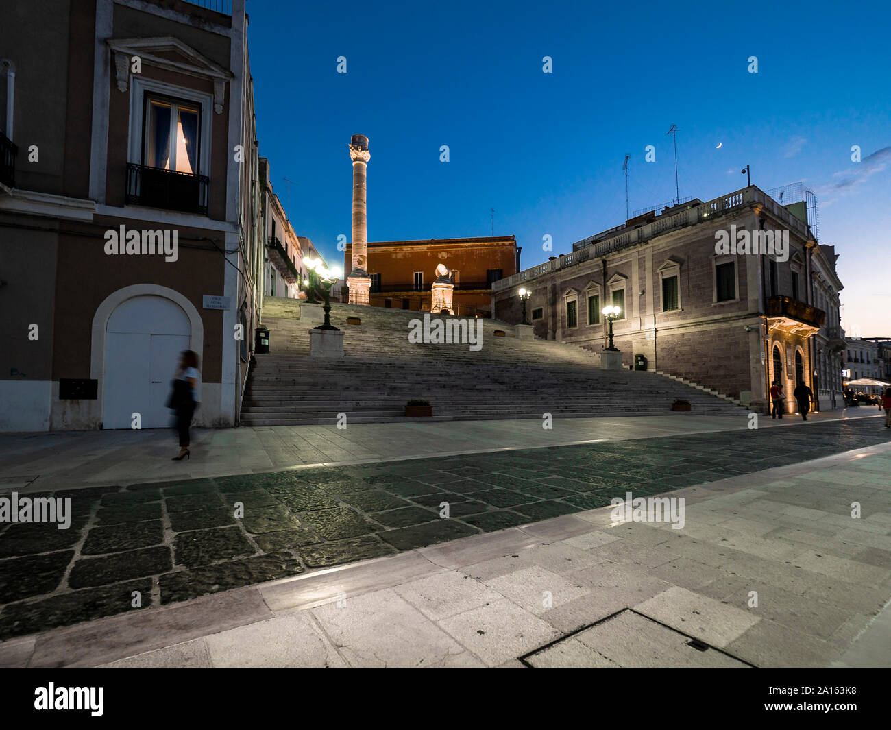 Columna Romana iluminada en pasos en medio de edificios en Brindisi contra el cielo en la noche Foto de stock