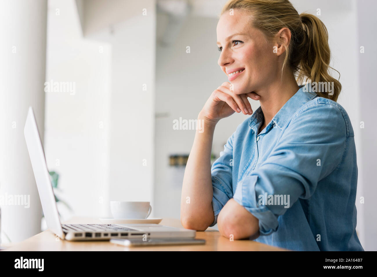 Mujer rubia sentada en la cafetería, utilización portátil Foto de stock
