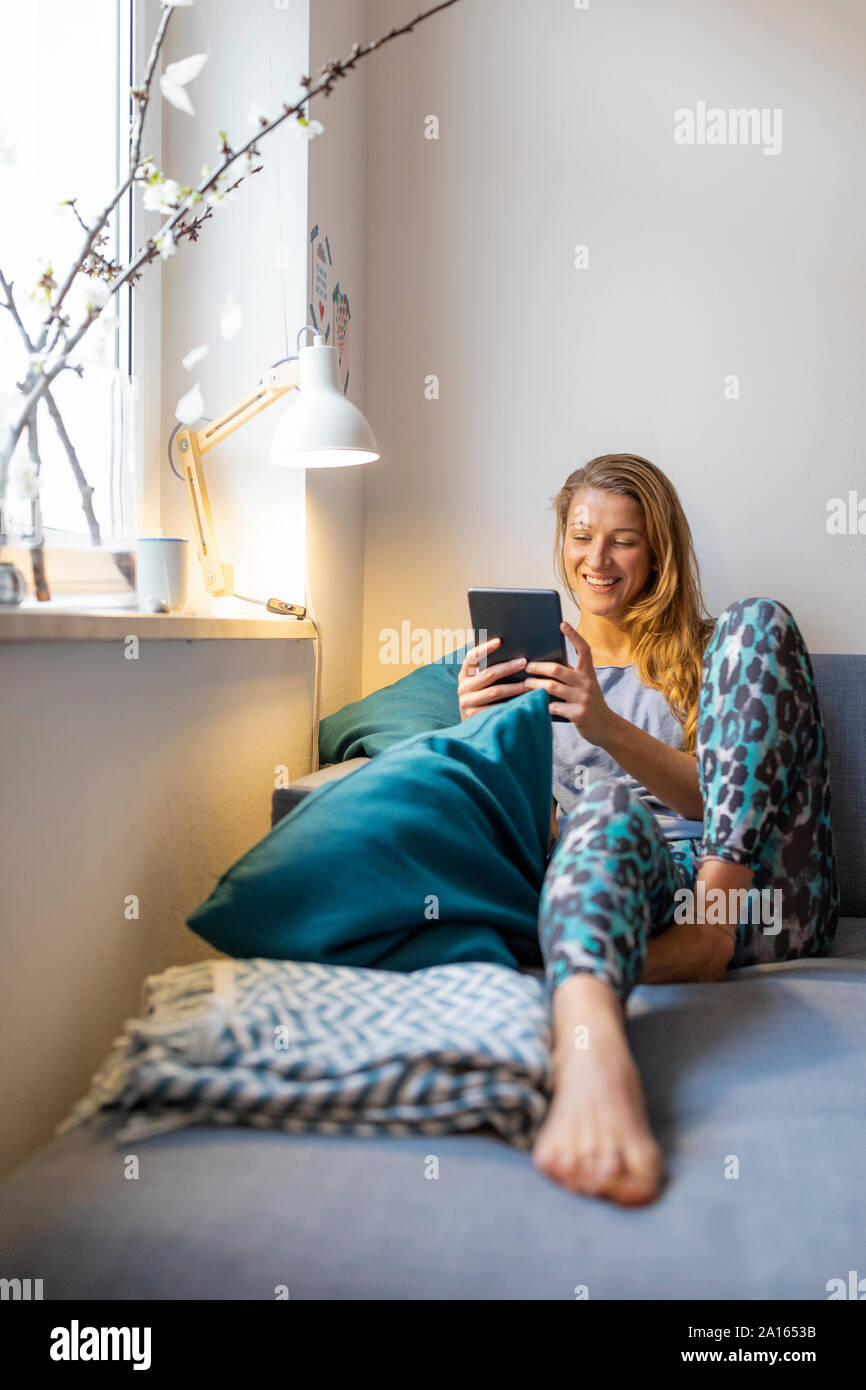 Feliz joven sentado en el sofá en casa utilizando tablet Foto de stock