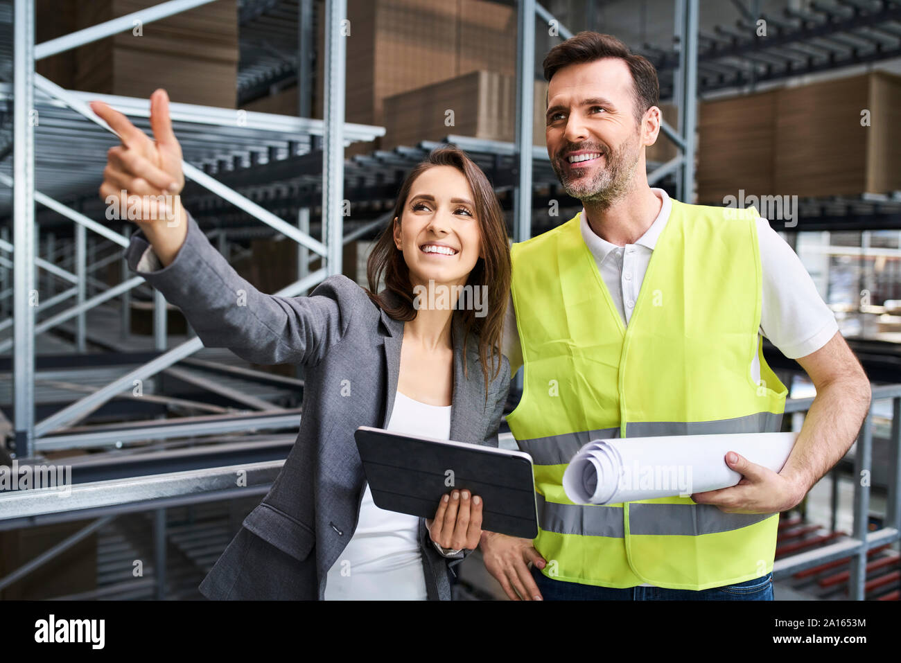 La empresaria sonriente hablar al hombre en chaleco reflectante de una fábrica. Foto de stock