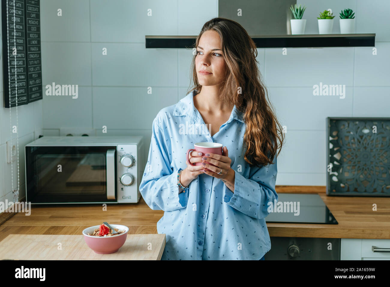 Retrato de joven mujer vistiendo pijama en cocina en casa sosteniendo una taza de café Foto de stock