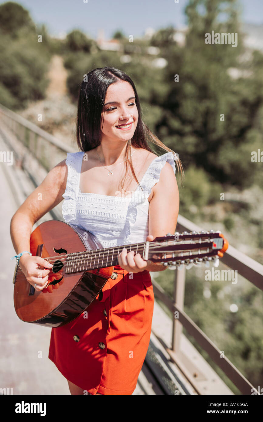 Mujer joven tocando la guitarra, de pie en el puente Foto de stock