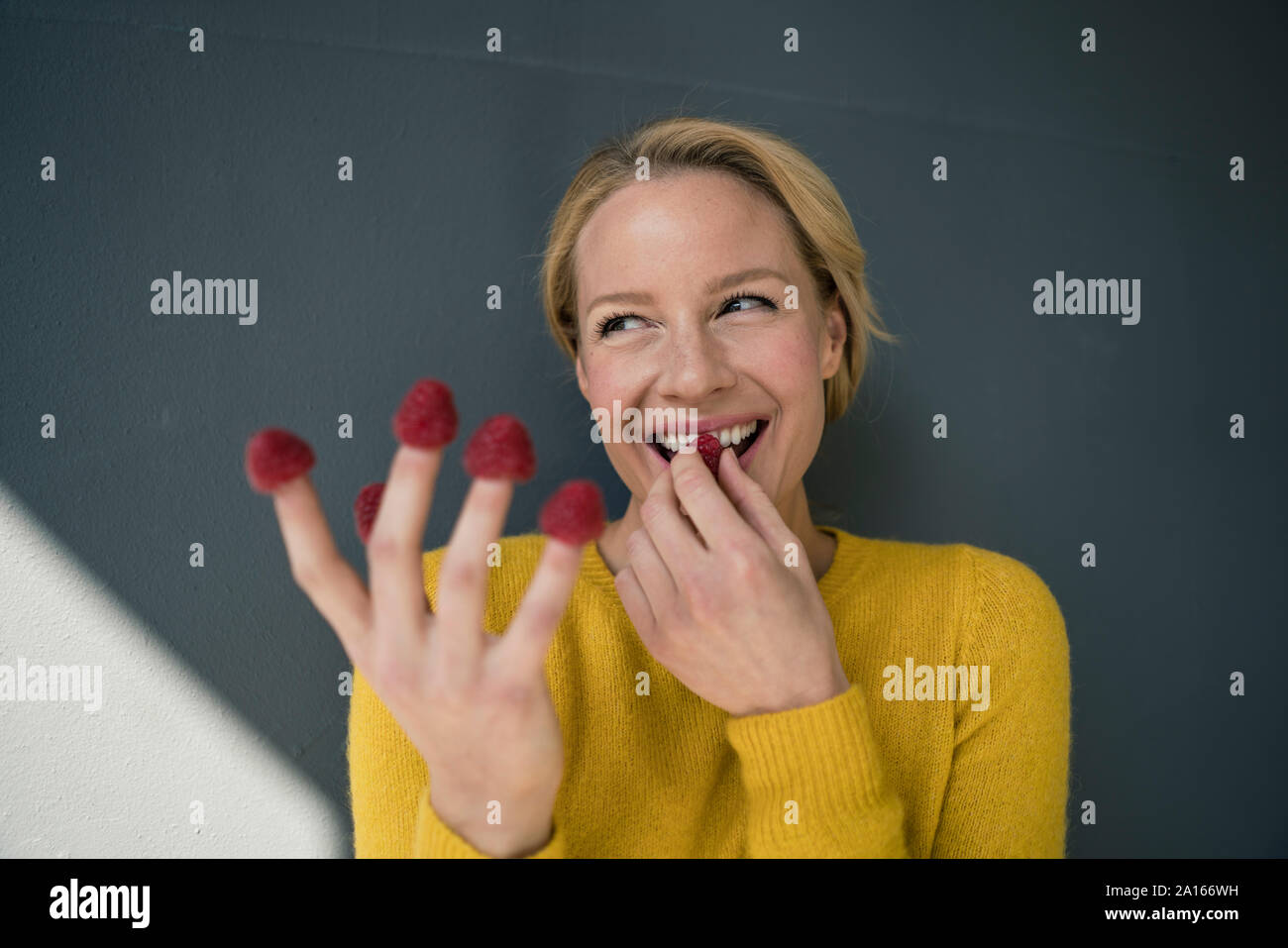 Mujer rubia con frambuesas sobre sus dedos, riendo Foto de stock