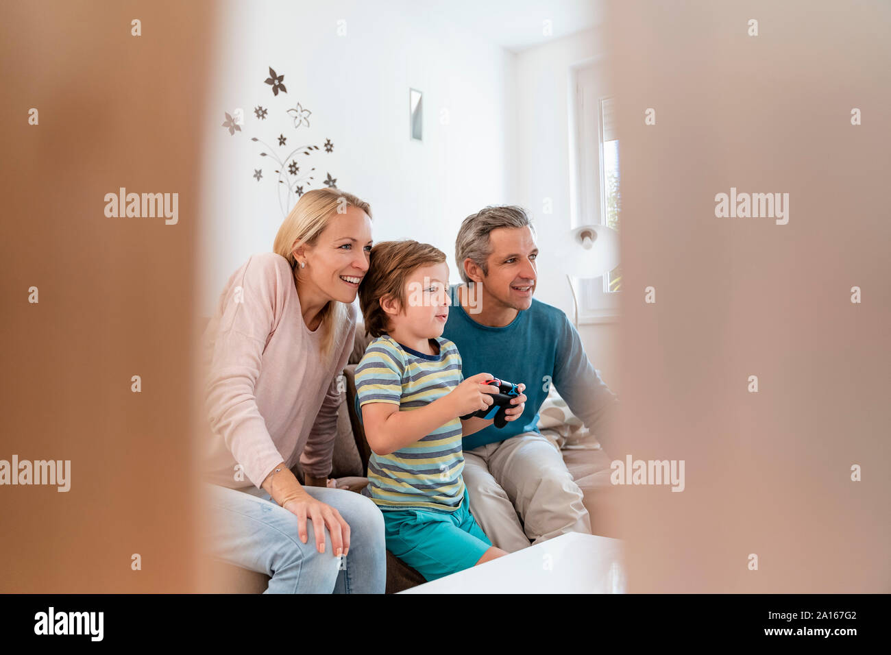 Felices padres con hijo jugar video juegos en sofá en casa Foto de stock