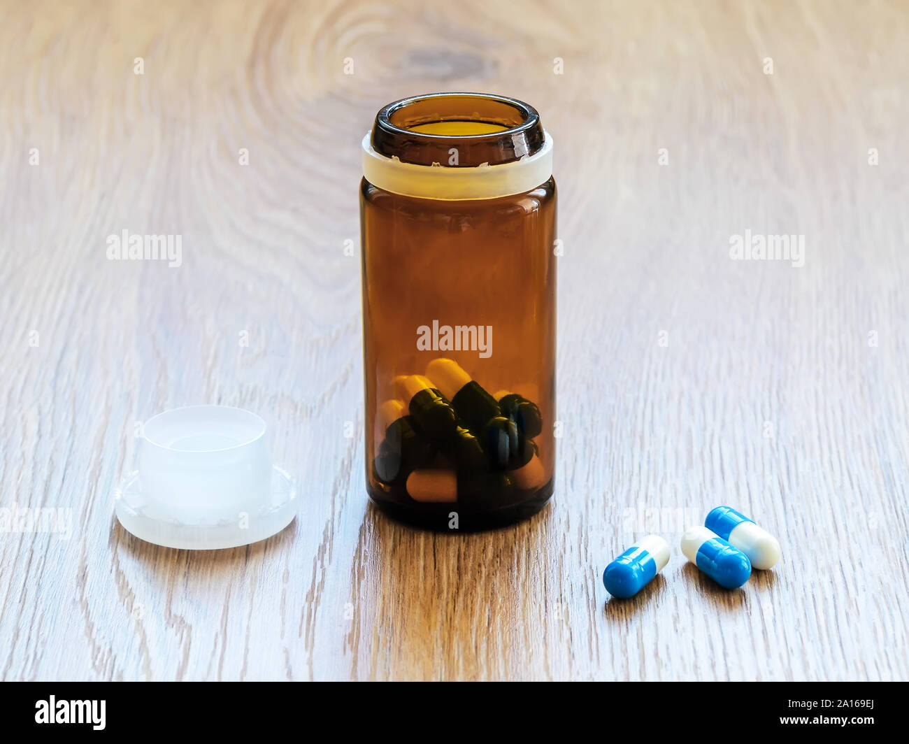 Las píldoras y jarra de cristal marrón con tapa en una tabla. Azul y blanca de cristal y cápsulas píldora botella en la superficie de madera marrón. A enfermarse y tomar las pastillas. Foto de stock
