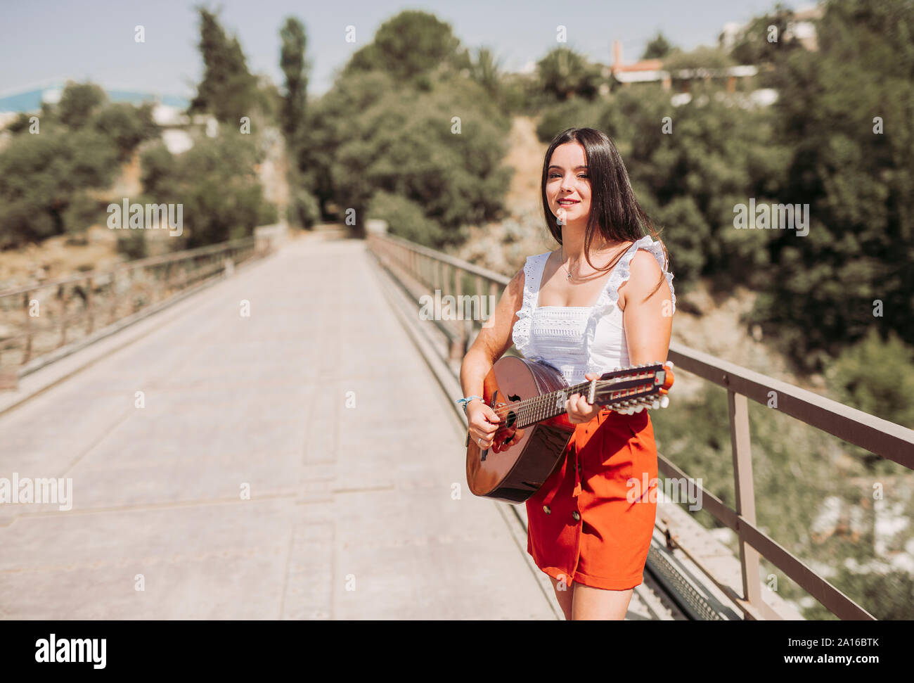 Mujer joven tocando la guitarra, de pie en el puente Foto de stock