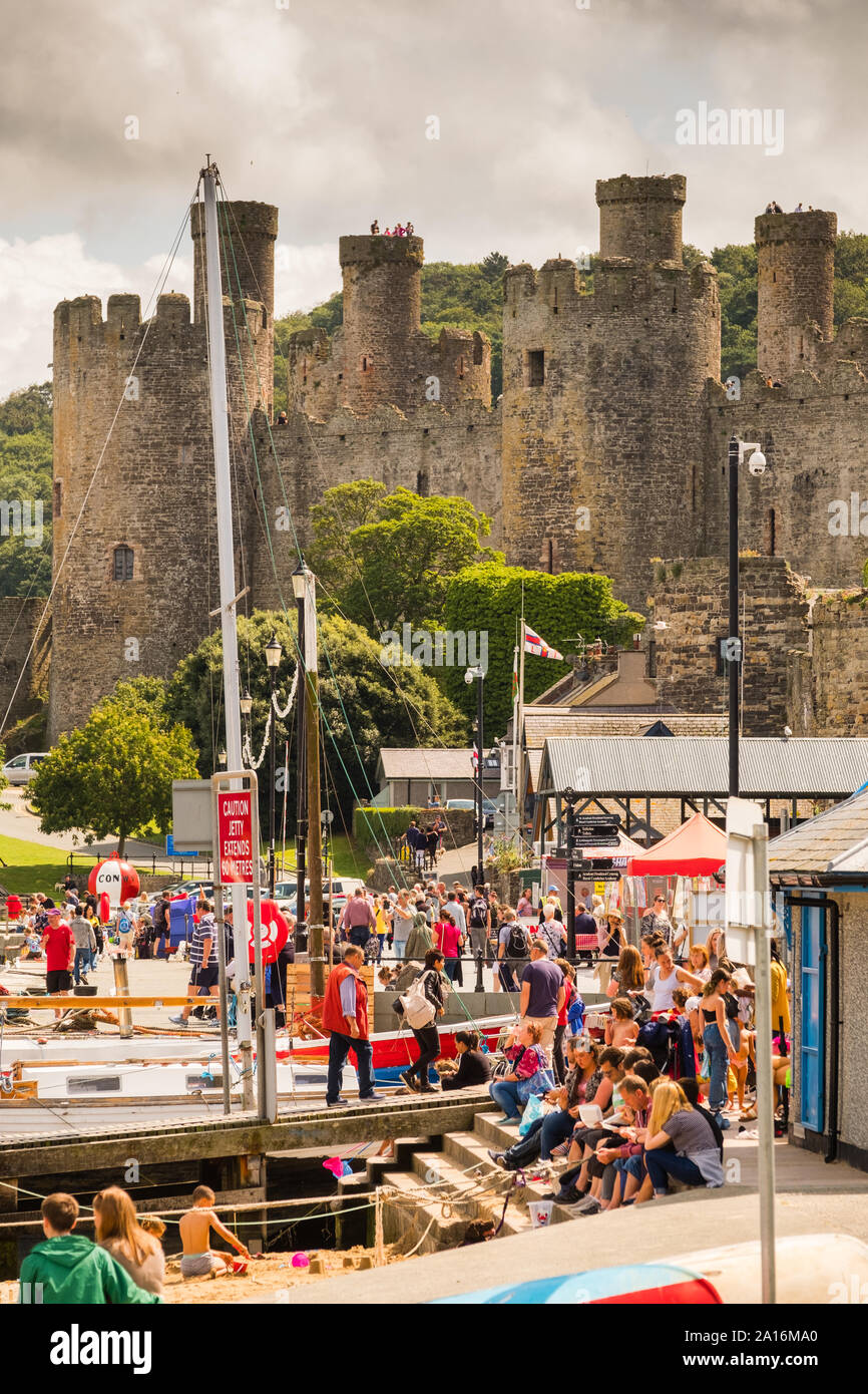Los turistas disfrutar de una cálida y soleada tarde de verano en el muelle a la sombra del castillo y la ciudad histórica de Conwy, [Conway] Gwynedd, al norte de Gales, Reino Unido Foto de stock