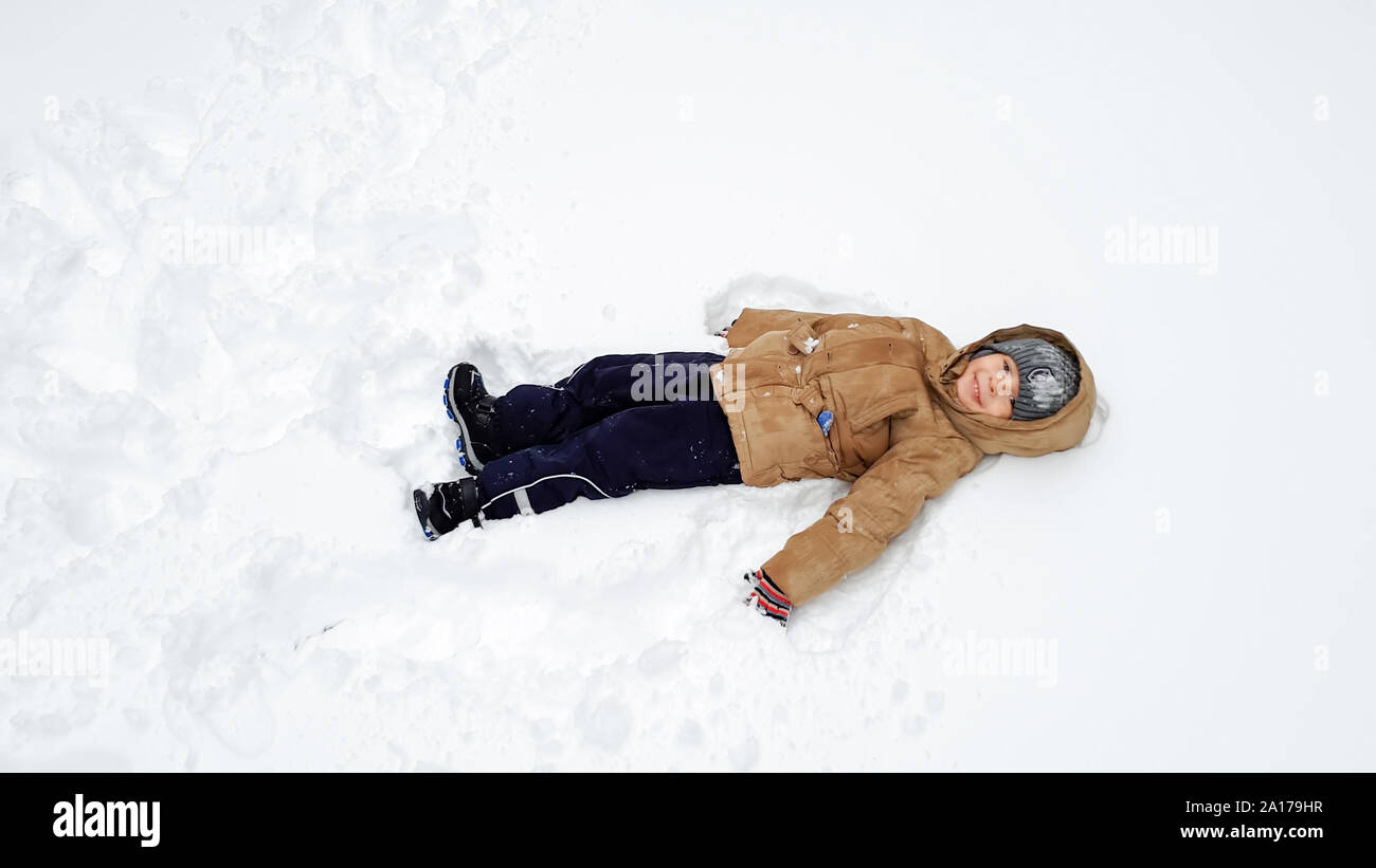 Imagen de chico lindo sonriente en escudo , han divertido jugando en la  nieve en el invierno, después de las nevadas. Juego de bolas de nieve en el  campo de juegos en