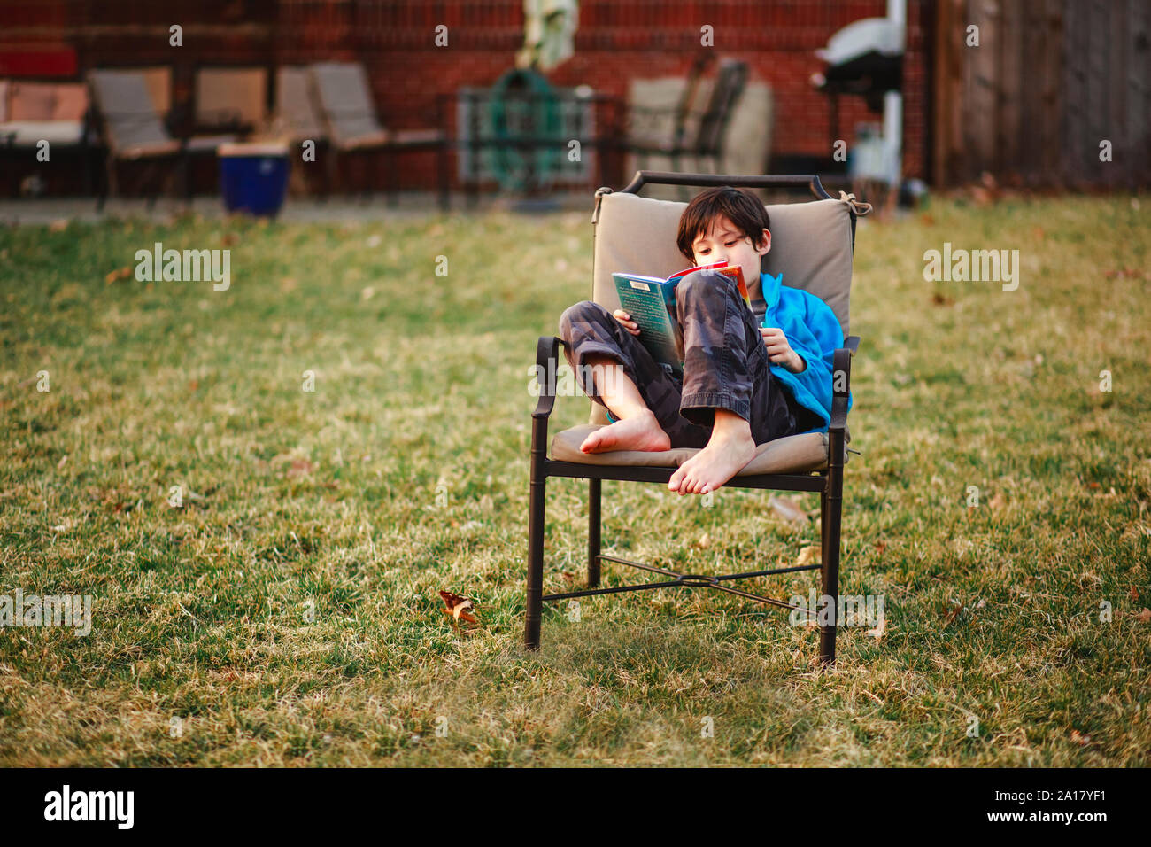 Un muchacho feliz lee un libro descalzo en patio en clima frío Foto de stock