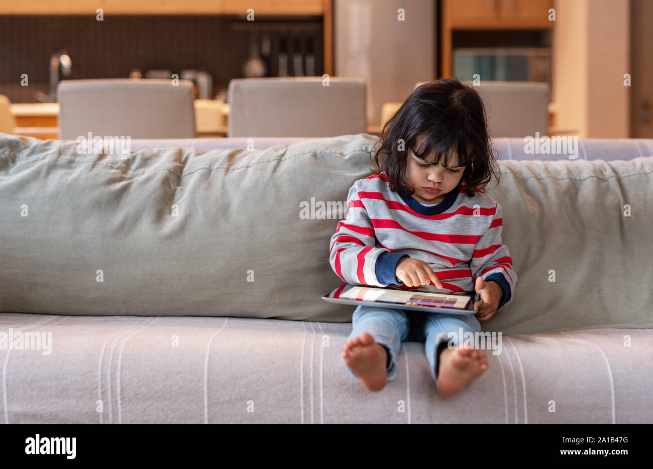 Niña sentada en su sofá con una tableta digital Foto de stock