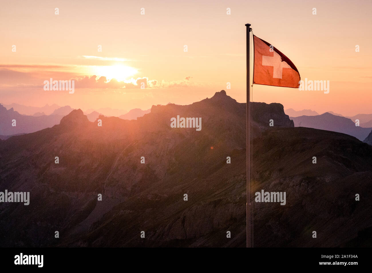 Bandera suiza retroiluminada al atardecer en los Alpes suizos Foto de stock