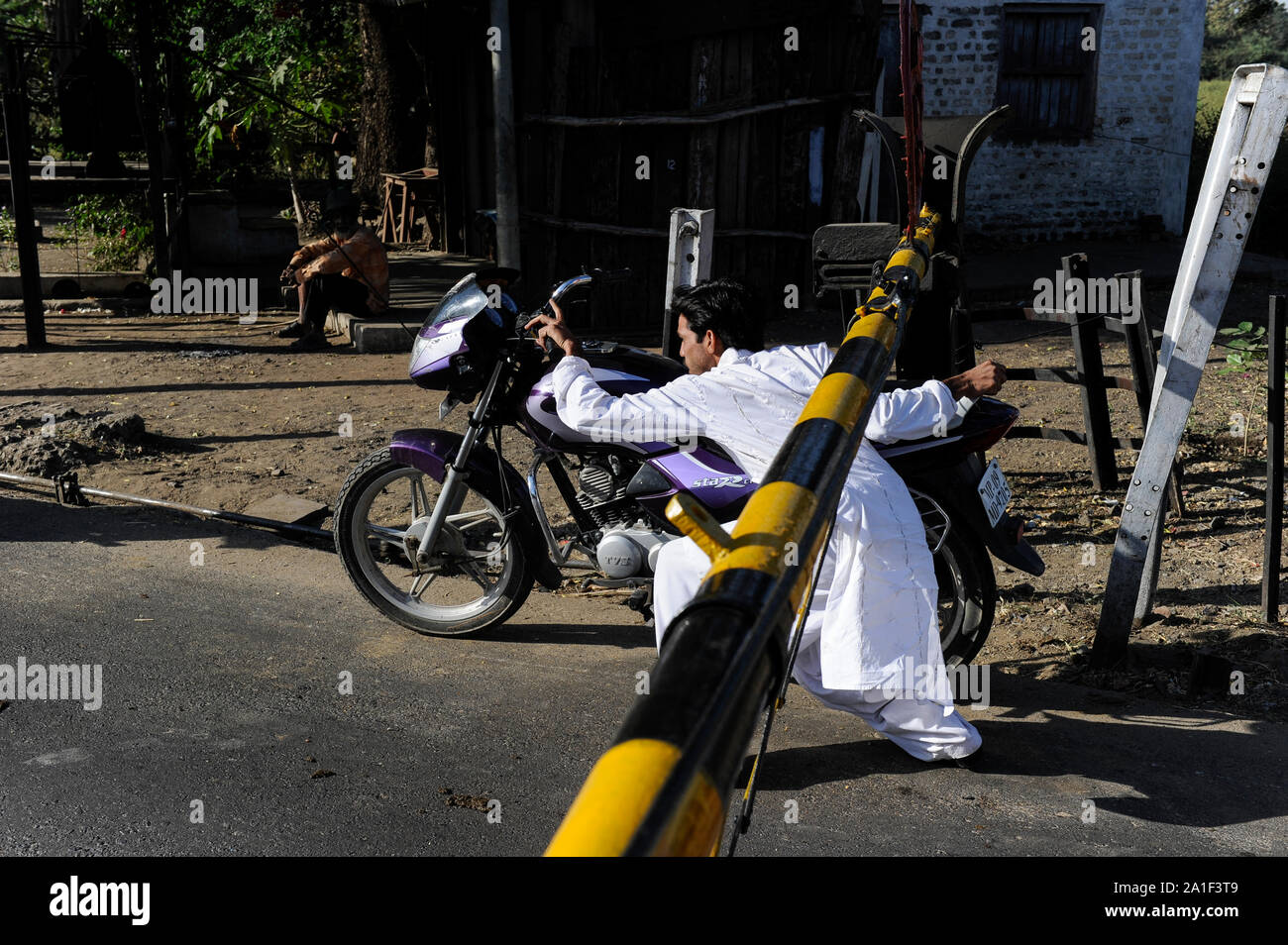 La India, Madhya Pradesh, región Khargone Nimad, conductor de moto, violan las normas de tráfico al cruzar un cruce ferroviario con barreras cerradas Foto de stock